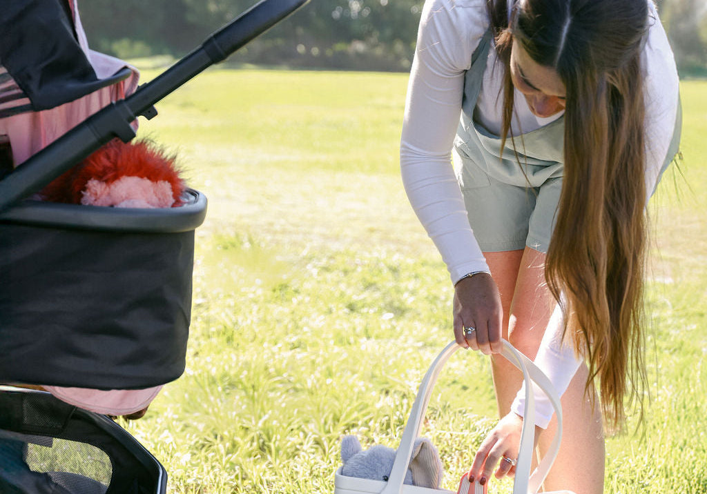 Parent organizing a diaper bag beside a stroller outdoors using whimSi silicone stroller clips to keep blankets and baby gear in place.