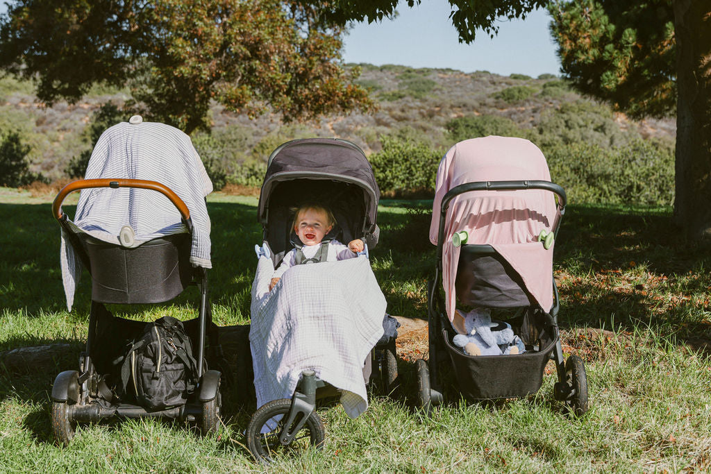 Three strollers side by side outdoors with blankets secured by whimSi clips