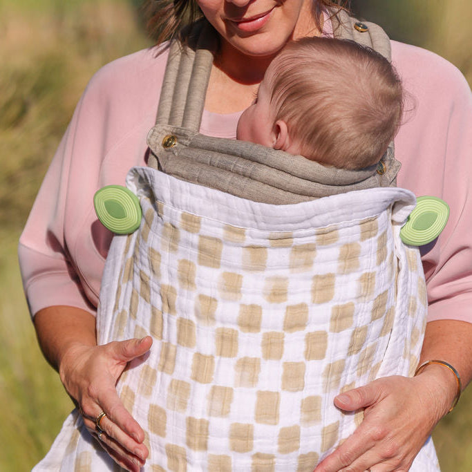 Mom babywearing using wind whimSi clips to keep blanket over baby for warmth