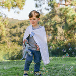 Child holding a blanket in place with whimSi clips play clips outdoors with bubbles and trees in the background